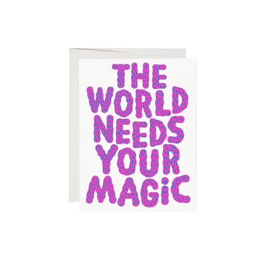 Pink and blue lettering on a white background reading "The World Needs Your Magic". The interior of the card is left blank, while the exterior is 100lb heavyweight card stock, with offset printing. Measuring 5.5 x 4.25 inches, the card features an illustration by Anke Weckmann and is printed in the USA on recycled paper.